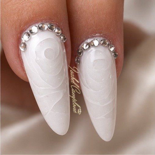Ongles blancs nacrés avec motif travaillé dans la matière et strass à la base, réalisation Isabel Camplone